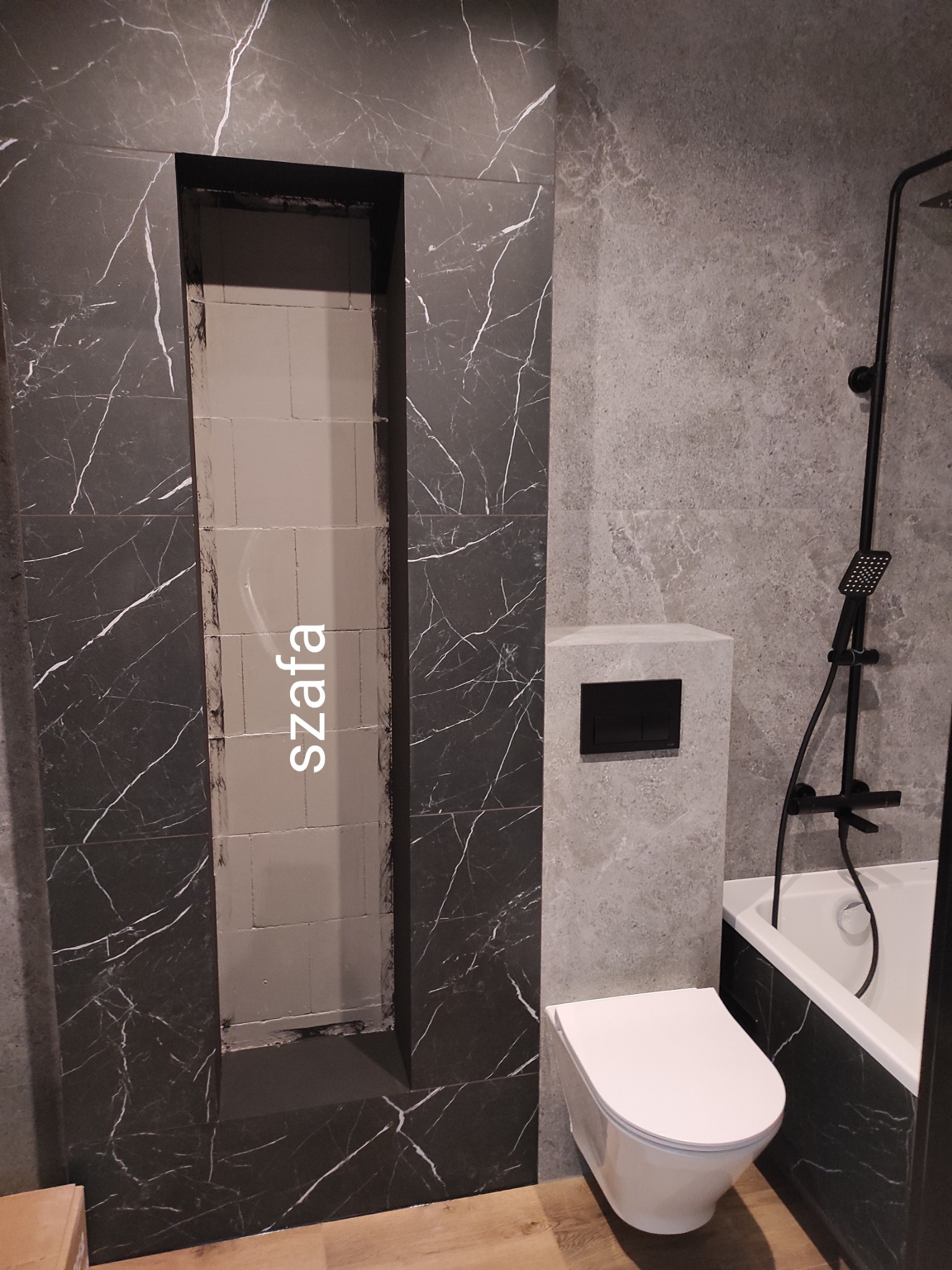 Nowoczesna łazienka z czarno-białymi marmurowymi płytkami, wbudowana półka w ścianie, biała toaleta wisząca i czarny zestaw prysznicowy przy wannie.