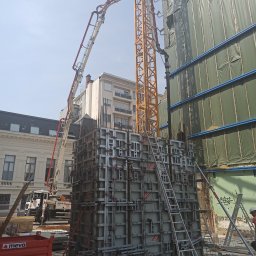Lewandowski Constructions Sp. z o.o. - Betonowanie fundamentów budynku w zabudowie miejskiej, widoczny szalunek, dźwig z pompą do betonu, oraz elementy zbrojenia.