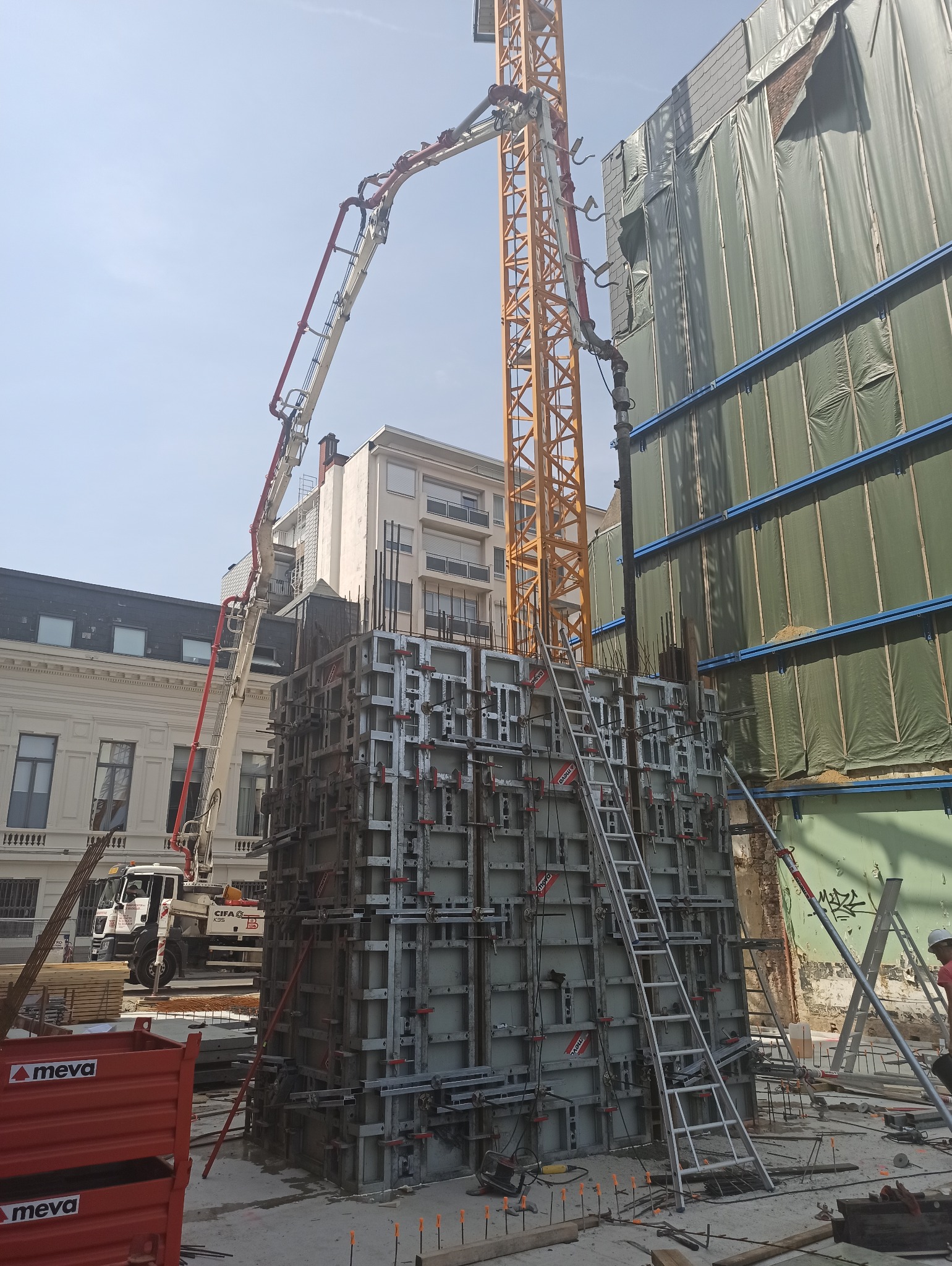 Betonowanie fundamentów budynku w zabudowie miejskiej, widoczny szalunek, dźwig z pompą do betonu, oraz elementy zbrojenia.