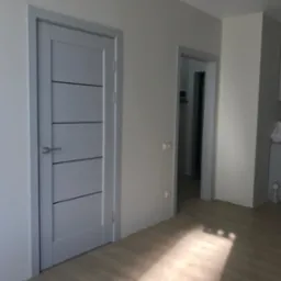 Szare drzwi wewnętrzne z poziomymi, ciemnymi paskami, zamontowane w jasnym pomieszczeniu z panelami podłogowymi, widok na otwarte drzwi do garderoby w tle.