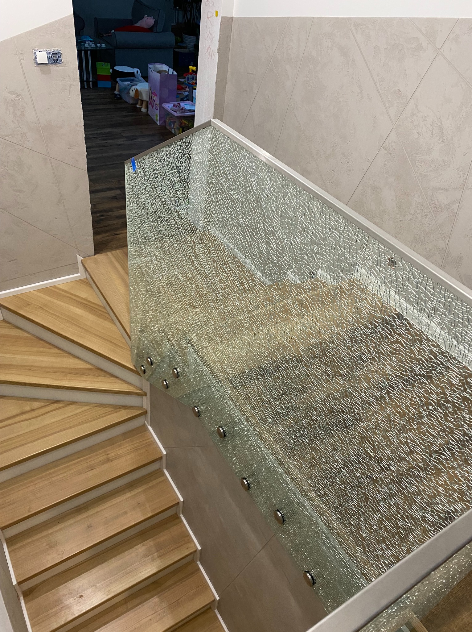 Drewniane schody z nowoczesną szklaną balustradą o fakturze kruszonego lodu, mocowaną punktowo. Widok z góry, jasne oświetlenie, neutralne tło.