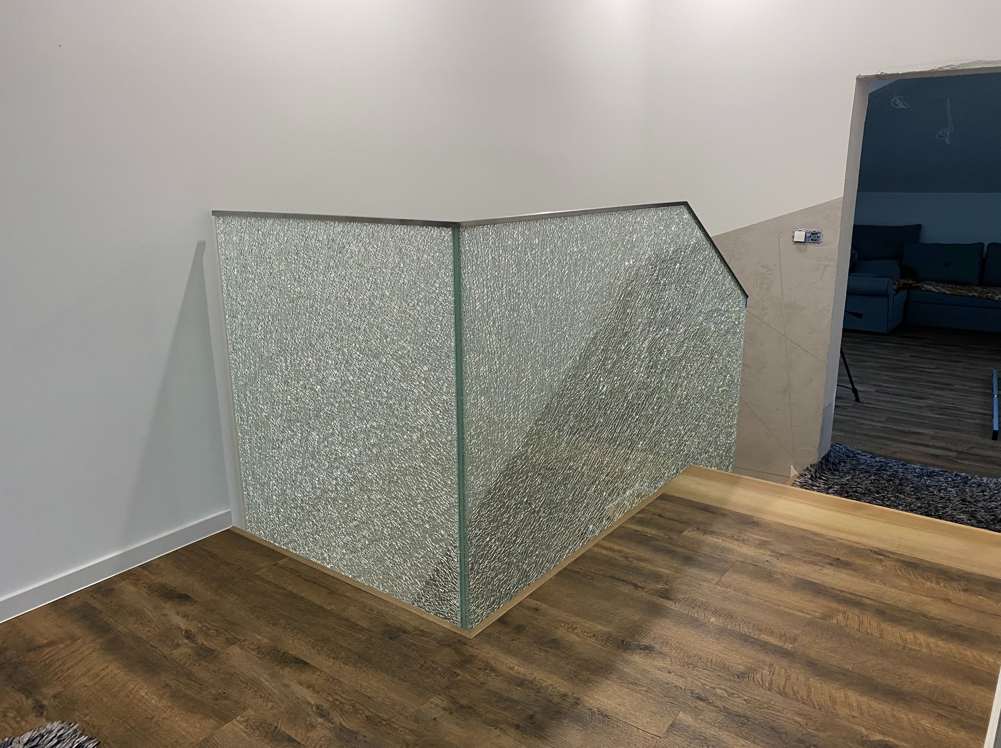 Szklana balustrada z metalowym wykończeniem, zamontowana na drewnianej podłodze wewnątrz budynku. Widoczne unikalne szkło o fakturze 'kora dębu'.