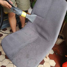 MODUS OPERANDI SPÓŁKA Z OGRANICZONĄ ODPOWIEDZIALNOŚCIĄ - Szara tapicerowana krzesło czyszczone parowo z użyciem odkurzacza Karcher, widoczne plamy na siedzisku przed czyszczeniem.