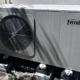 F.H.U Taurus Tadeusz Kuśpiel - Zewnętrzna jednostka pompy ciepła Ferroli, zamontowana na betonowych podstawach, widoczne elementy instalacji i logo producenta.