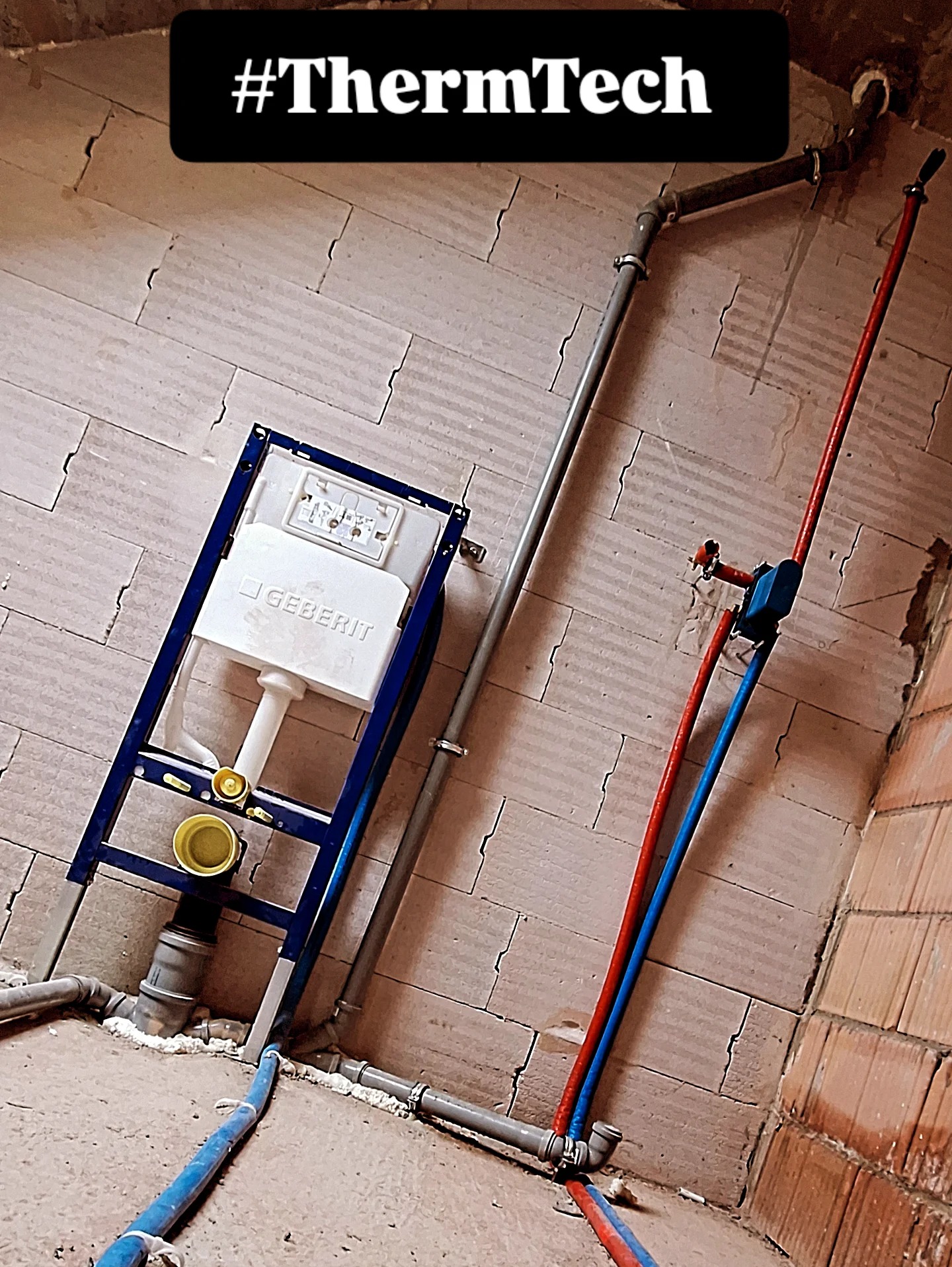 Instalacja podtynkowa Geberit z rurami PEX w kolorach czerwonym i niebieskim, szara rura kanalizacyjna, ściany w trakcie wykończenia, widoczne łączenia i mocowania.