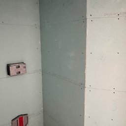 Perfect Line ARKADIUSZ MYSZAK - Wewnętrzny narożnik pomieszczenia wykończony płytami kartonowo-gipsowymi, widoczne puszki instalacyjne i ślady po wkrętach, surowy stan przed dalszymi pracami wykończeniowymi.