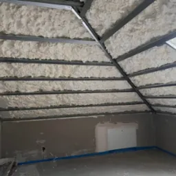 Poddasze z izolacją natryskową pianką PUR, widoczne metalowe profile konstrukcji. Ściany w szarym kolorze, przygotowane pod dalsze prace wykończeniowe.