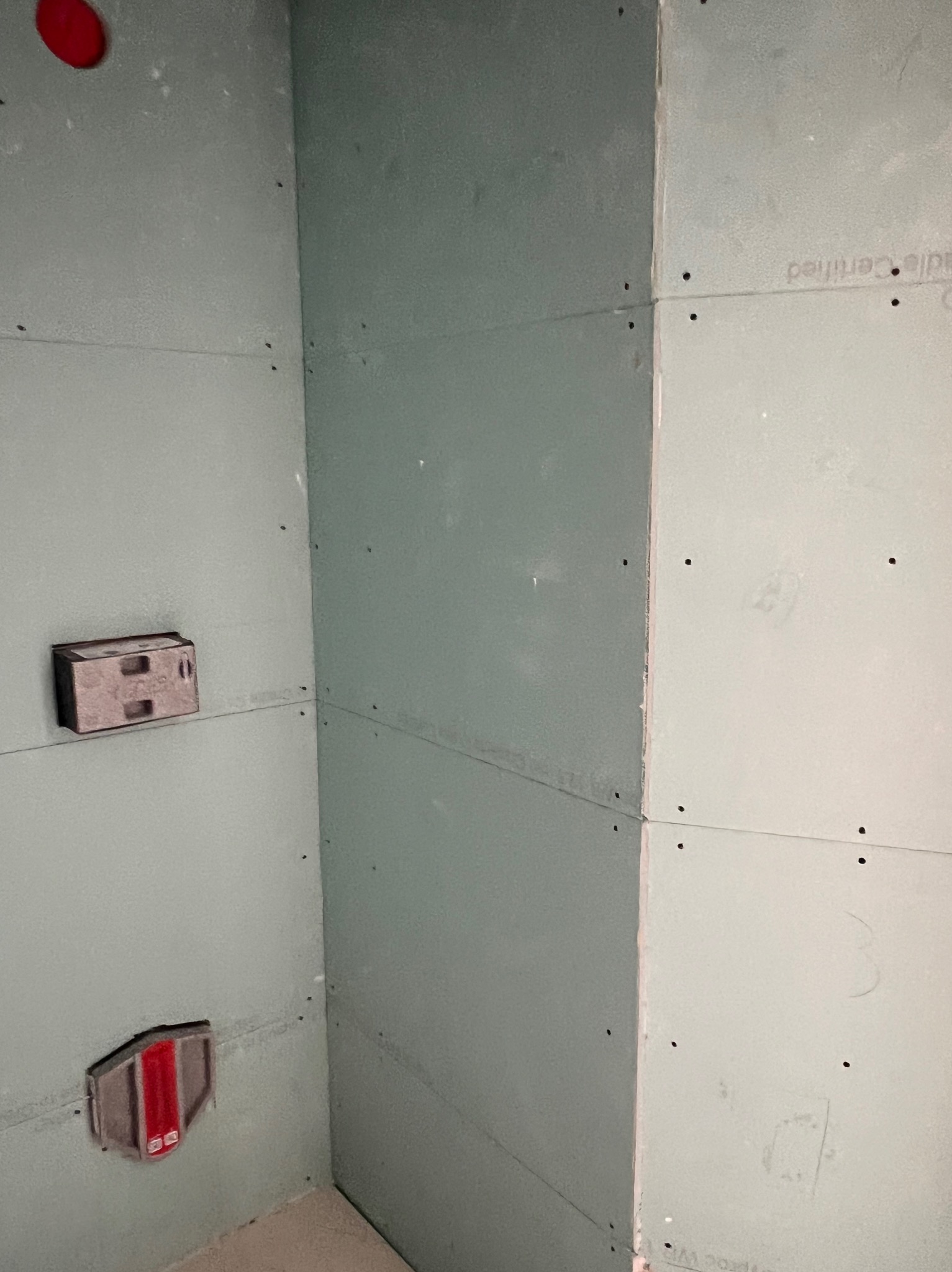 Wewnętrzny narożnik pomieszczenia wykończony płytami kartonowo-gipsowymi, widoczne puszki instalacyjne i ślady po wkrętach, surowy stan przed dalszymi pracami wykończeniowymi.