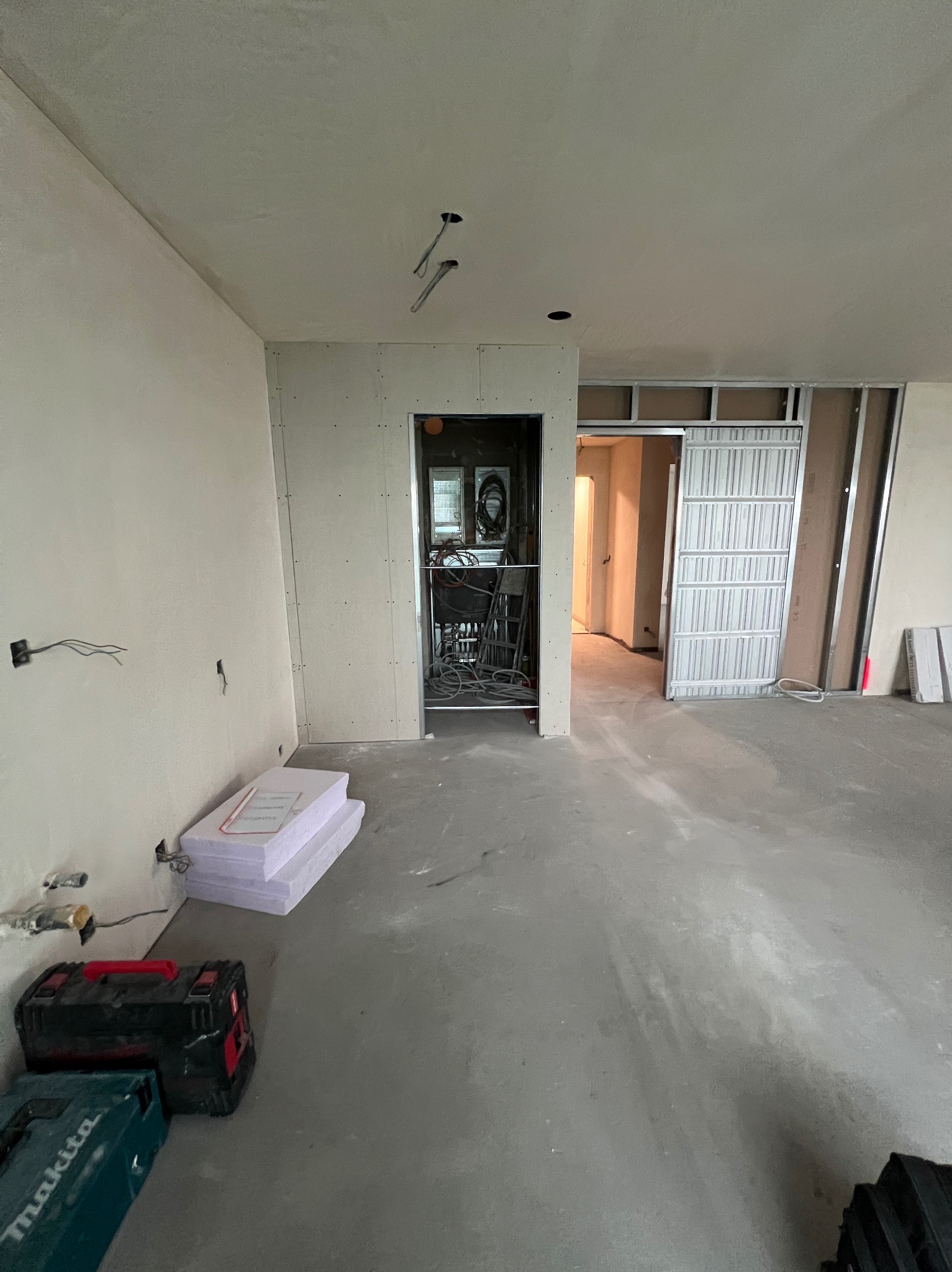 Wnętrze w trakcie prac wykończeniowych: ściany z płyt kartonowo-gipsowych, widoczne profile metalowe, podłoga wylewka, narzędzia i materiały budowlane w pomieszczeniu, przygotowane punkty elektryczne.