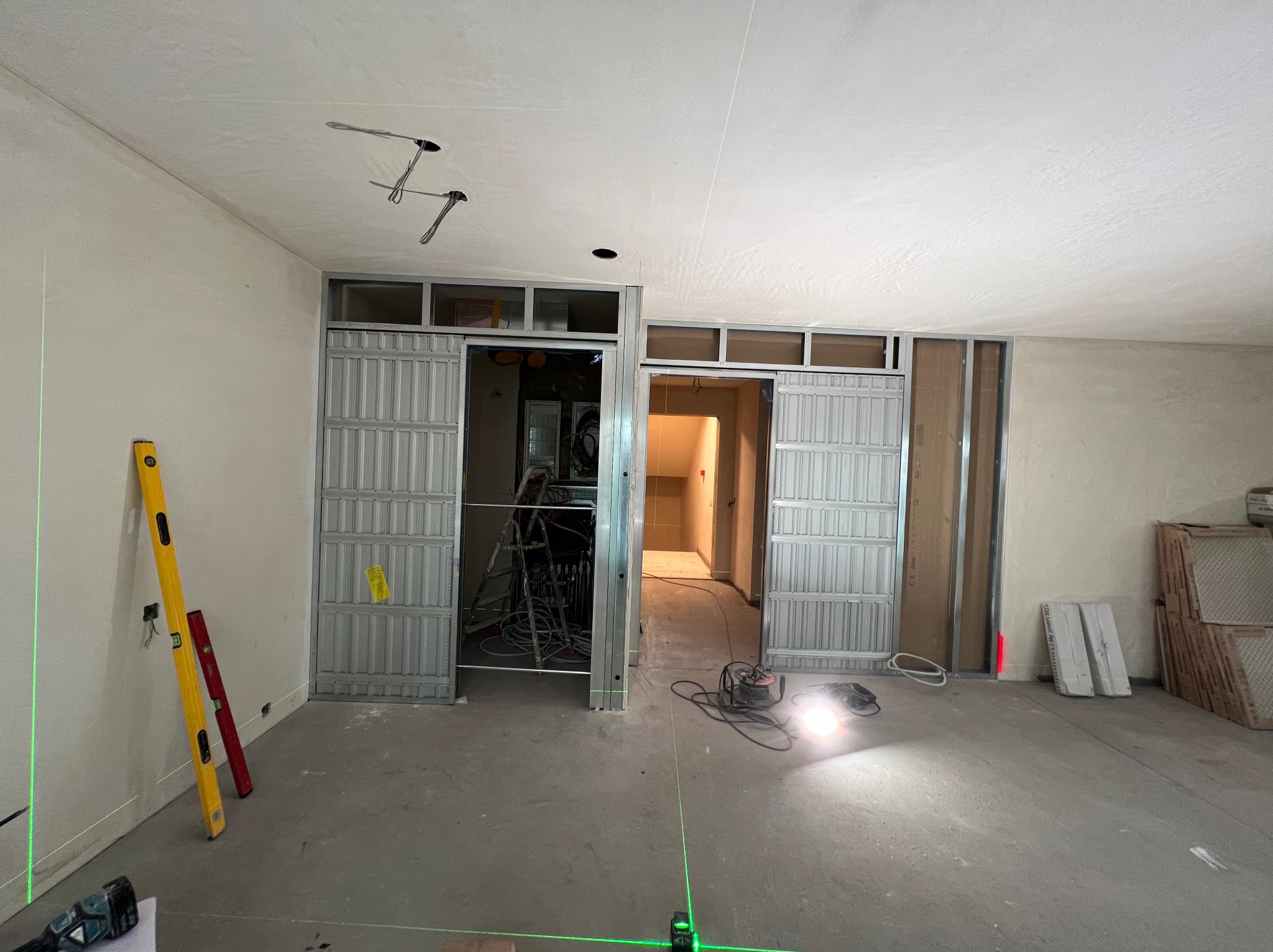 Montaż metalowego stelażu pod ściankę działową z płyt kartonowo-gipsowych, widoczne poziomice i laser krzyżowy, surowy stan wnętrza.