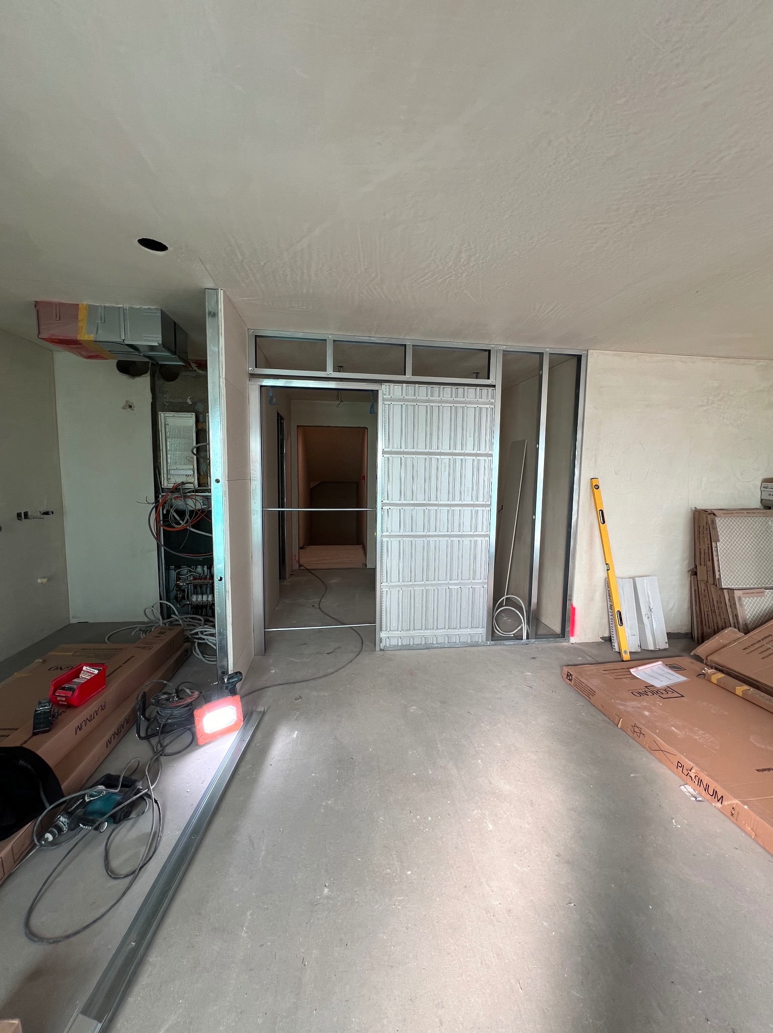 Wnętrze w trakcie remontu: widoczne profile metalowe konstrukcji ścianki działowej z drzwiami przesuwnymi, instalacja elektryczna, narzędzia i materiały budowlane na podłodze, ściany przygotowane...