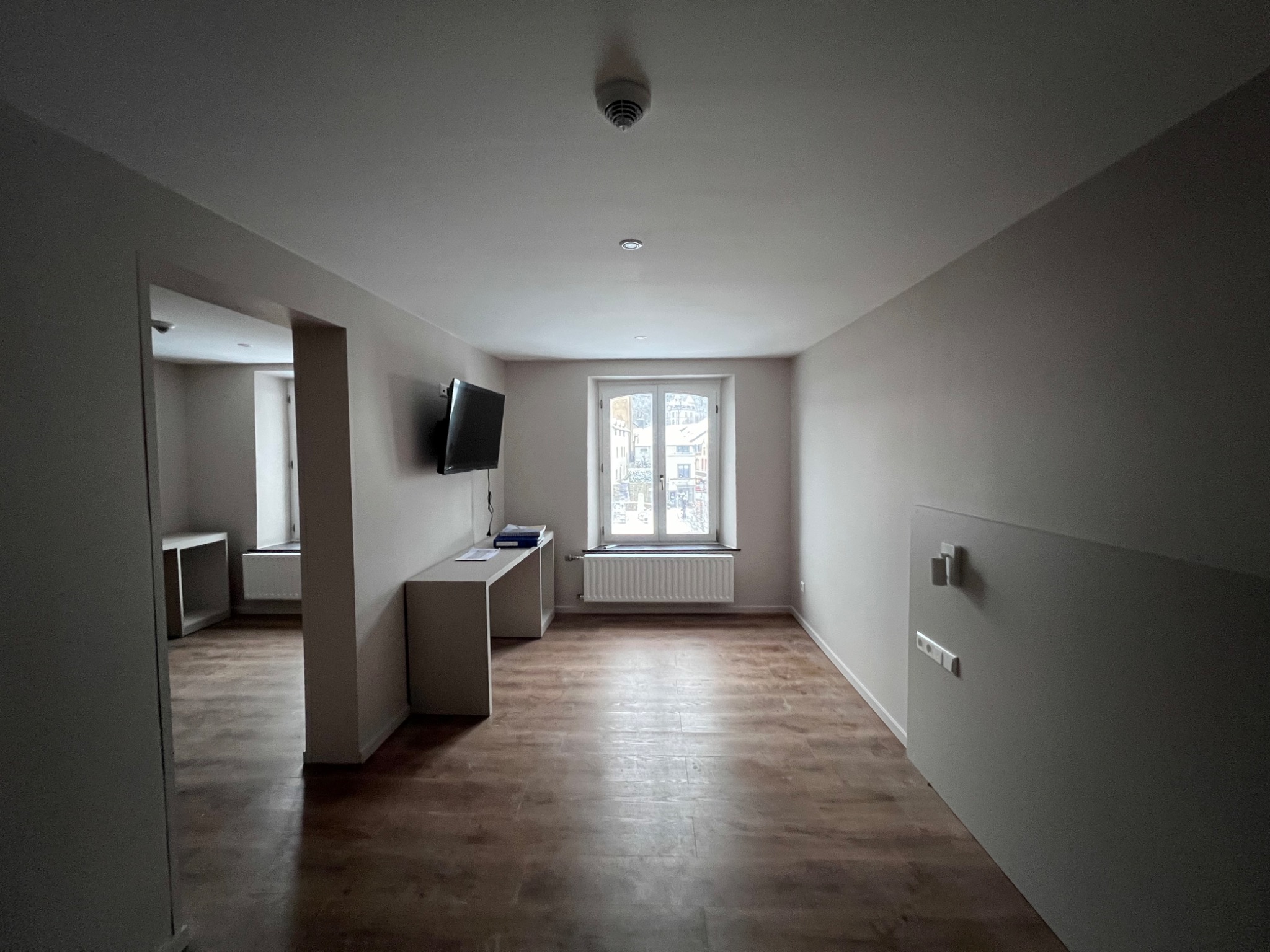 Wnętrze pokoju po remoncie z drewnopodobną podłogą, świeżo pomalowanymi ścianami i zamontowanym telewizorem na ścianie.