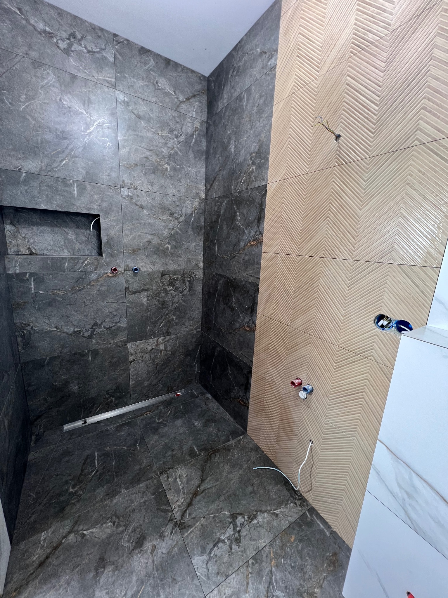 Łazienka w trakcie wykańczania: ciemne płytki imitujące marmur na ścianach i podłodze, kontrastujące z jasnymi płytkami w jodełkę na fragmencie ściany.