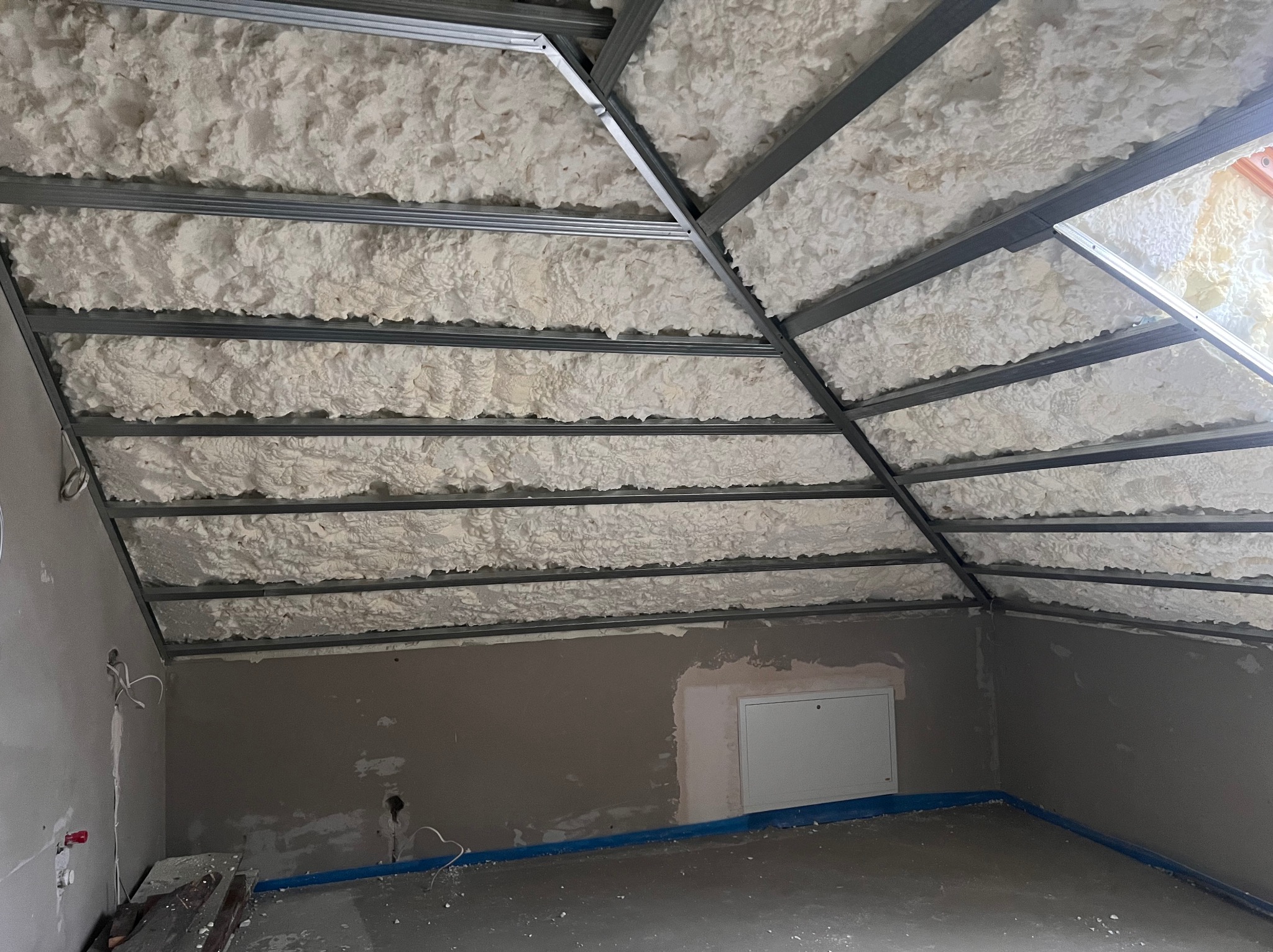 Poddasze z izolacją natryskową pianką PUR, widoczne metalowe profile konstrukcji. Ściany w szarym kolorze, przygotowane pod dalsze prace wykończeniowe.