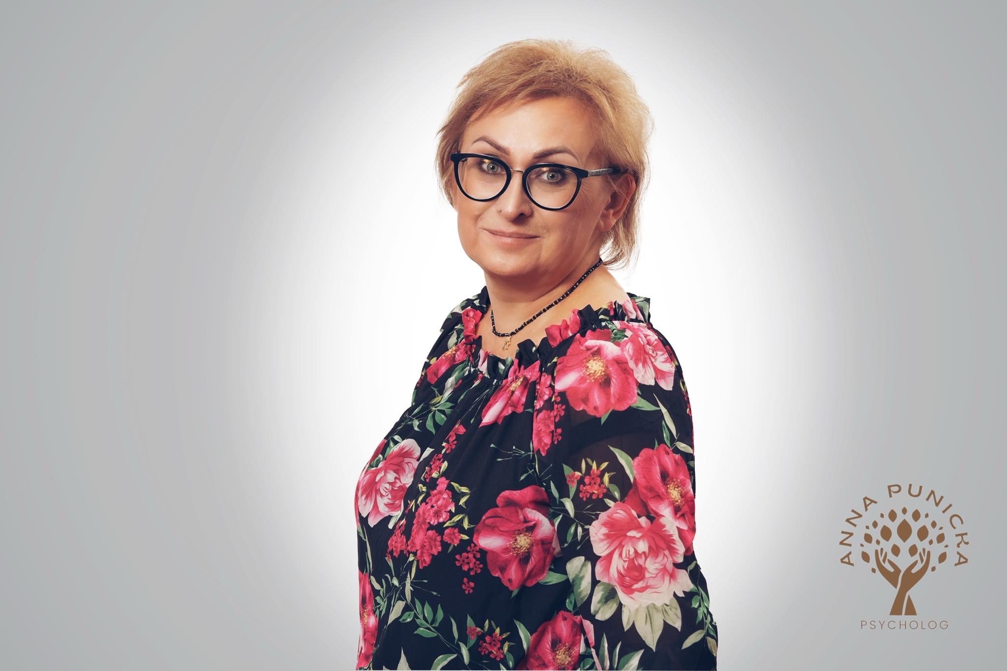 Portret uśmiechniętej kobiety w okularach i kwiecistej bluzce, obok logo psychologa z drzewem i dłońmi na szarym tle.