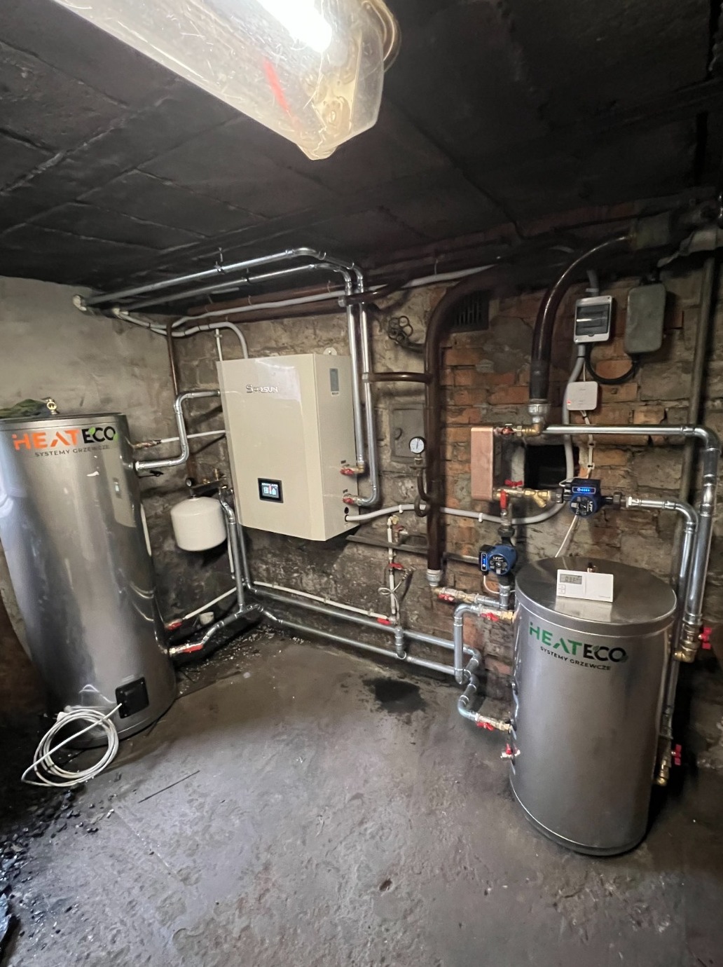 Instalacja grzewcza w piwnicy z kotłem gazowym i dwoma zbiornikami ciepłej wody użytkowej marki HEATECO, widoczne rury i armatura.