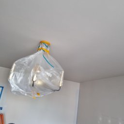 Ruslan - Lampa sufitowa zabezpieczona folią i taśmą malarską podczas prac malarskich, widoczny fragment ściany po nałożeniu gładzi.