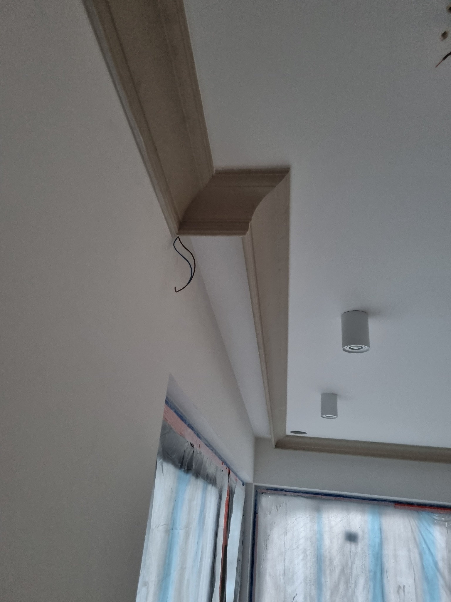 Wykończenie sufitu z dekoracyjną listwą przysufitową, widoczne przygotowanie do malowania okna folią ochronną i wystające przewody elektryczne.