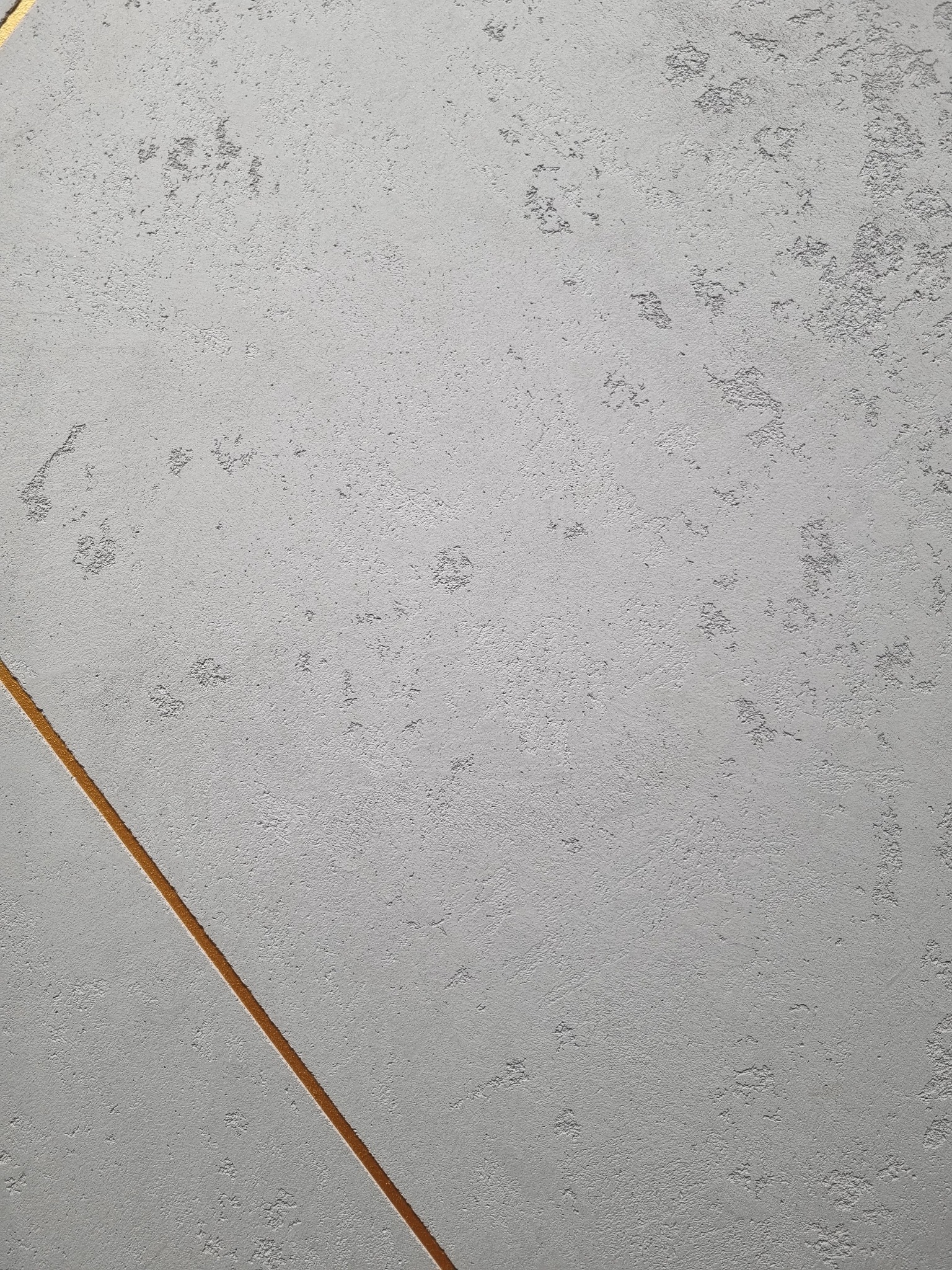 Szara ściana z dekoracyjną strukturą i złotym paskiem biegnącym ukośnie.