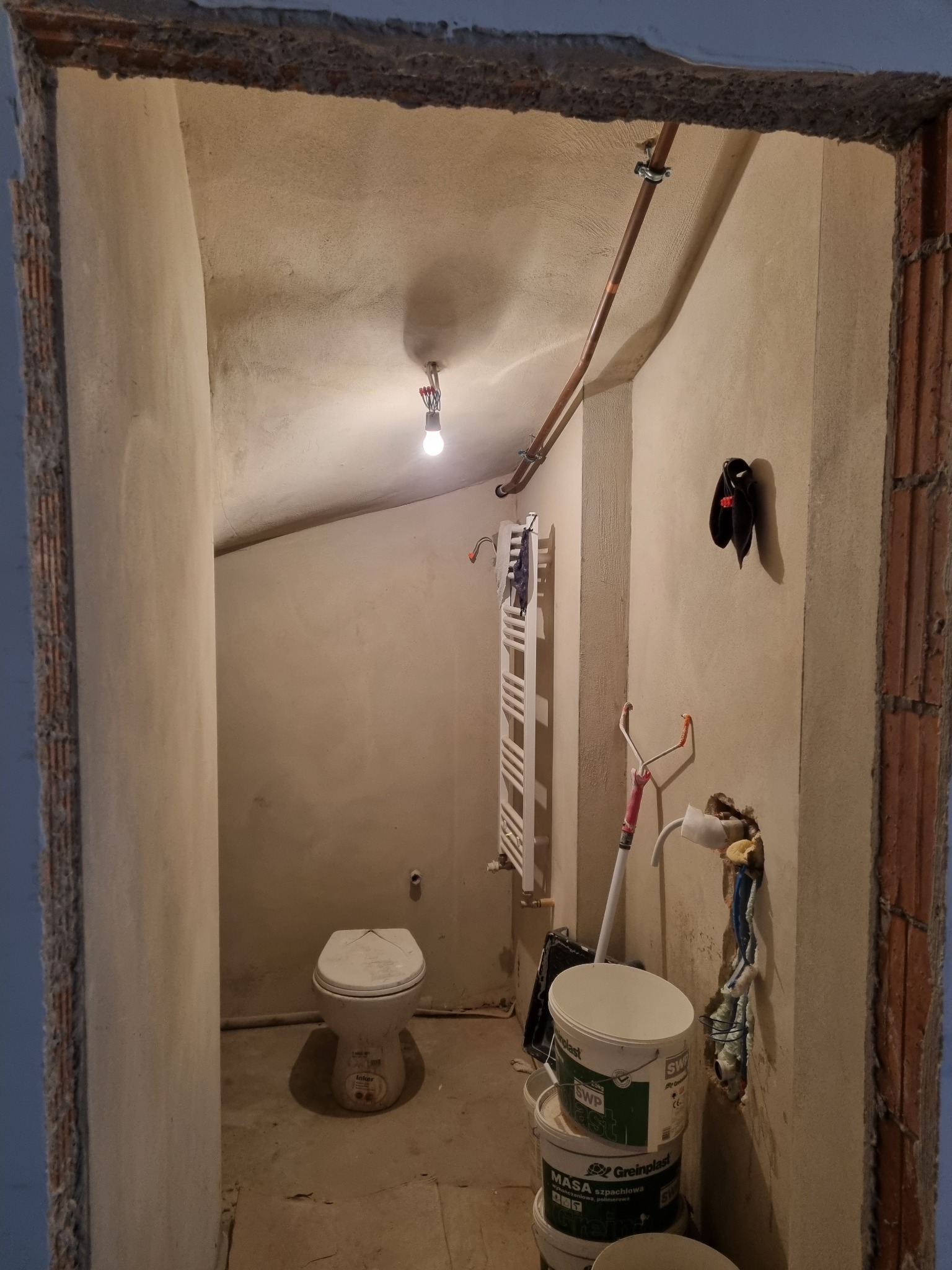 Łódź: Łazienka w trakcie remontu, widoczne surowe ściany, instalacja hydrauliczna, grzejnik drabinkowy, toaleta i wiadra z masą szpachlową.