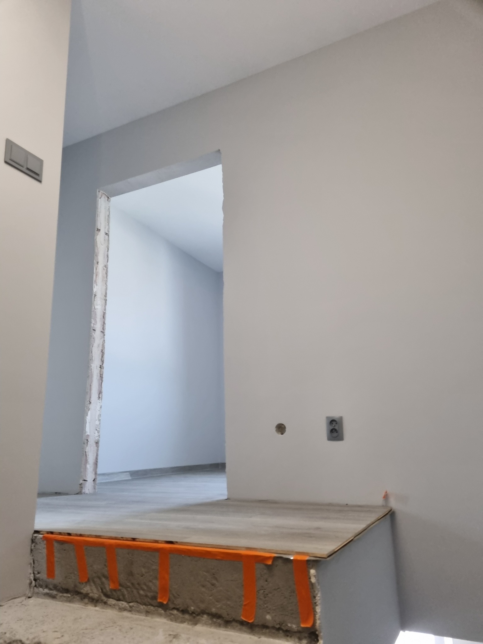 Przygotowanie podłogi w nowym mieszkaniu: wylewka z pomarańczowymi paskami poziomującymi, widoczne gniazdka elektryczne i surowy otwór drzwiowy.