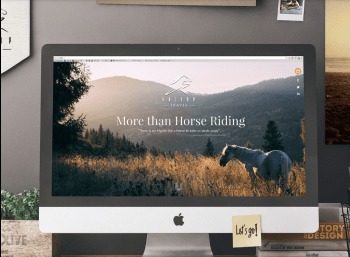 Ekran komputera iMac wyświetlający stronę internetową z motywem jeździeckim: krajobraz z koniem, logo z motywem górskim i napis 'More than Horse Riding'. Na biurku roślina w doniczce i książki.
