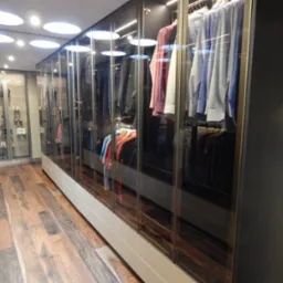 Długa szafa wnękowa z przeszklonymi drzwiami przesuwnymi, oświetleniem LED wewnątrz i drewnianą podłogą w tle.