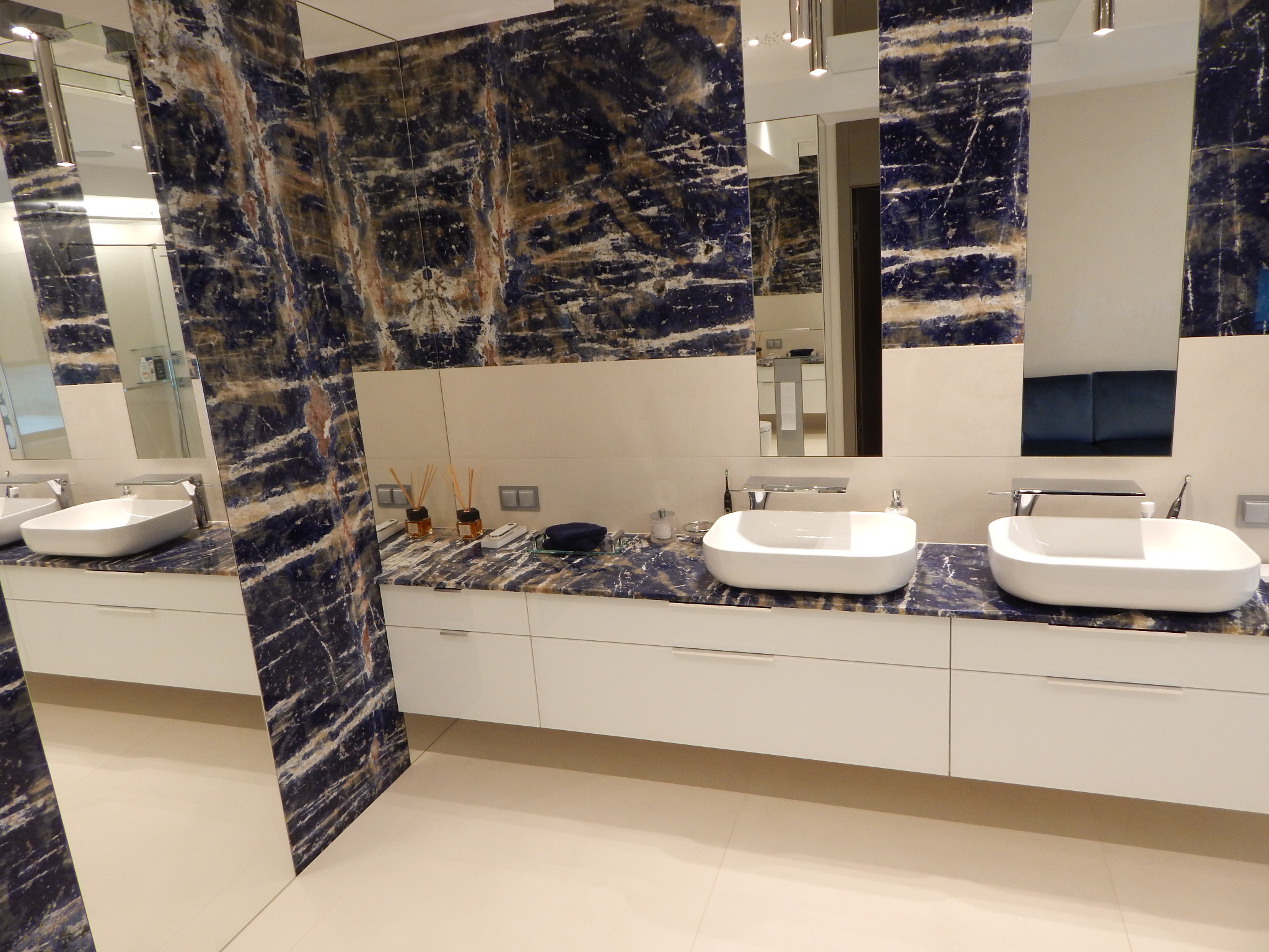 Elegancka, nowoczesna łazienka we Wrocławiu z blatem z ciemnego kamienia o unikalnym wzorze, białymi szafkami pod umywalkami i dużymi lustrami.