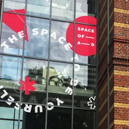 Na Wczoraj - Zewnętrzna grafika na szklanej fasadzie budynku z napisem 'THE SPACE OF A-D ENJOY YOURSELF' oraz czerwonymi elementami geometrycznymi, widoczny budynek z cegły w tle.