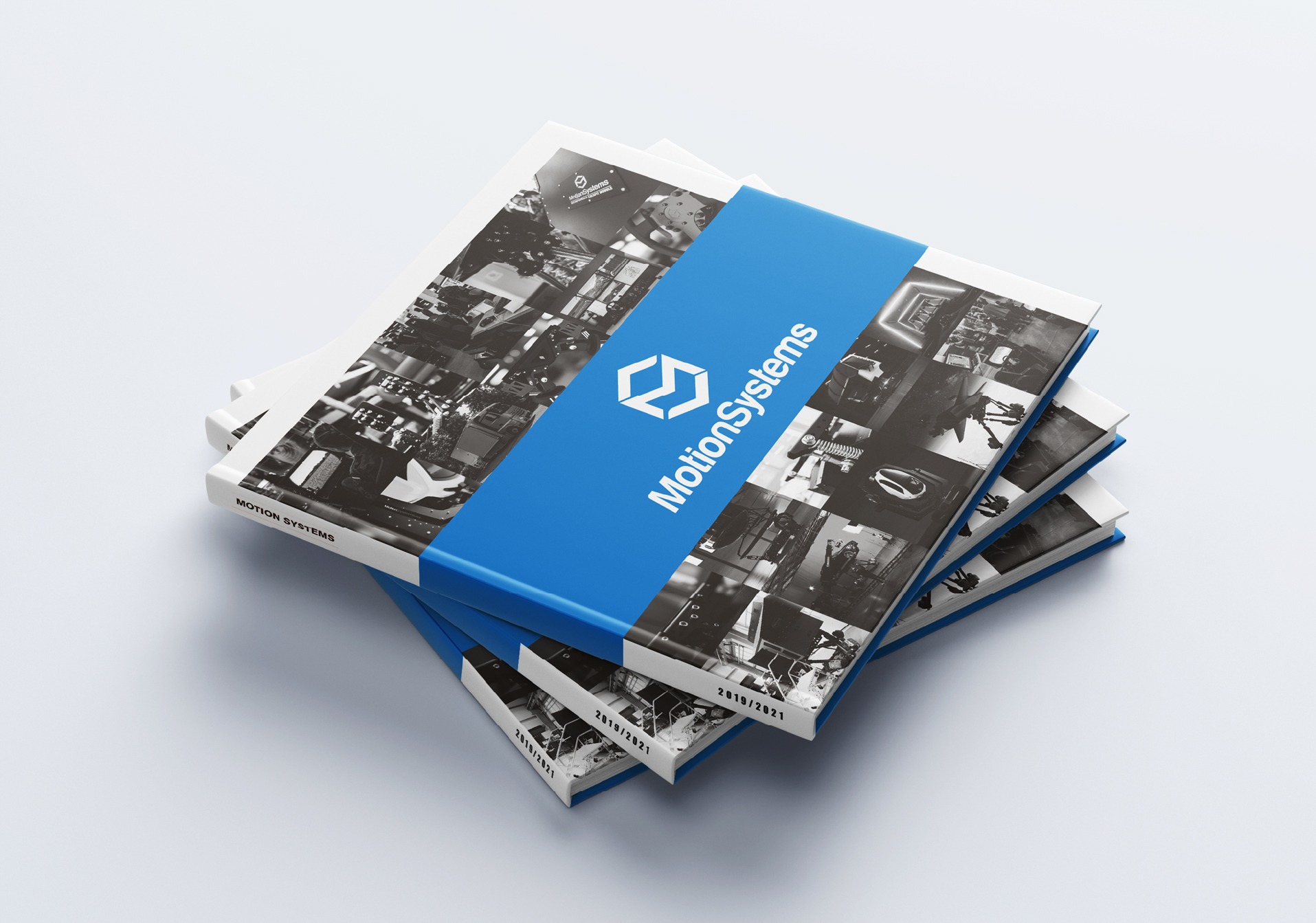 Stos trzech katalogów firmowych MotionSystems z niebieskim paskiem, zawierających czarno-białe zdjęcia maszyn i urządzeń, leżących na białym tle.