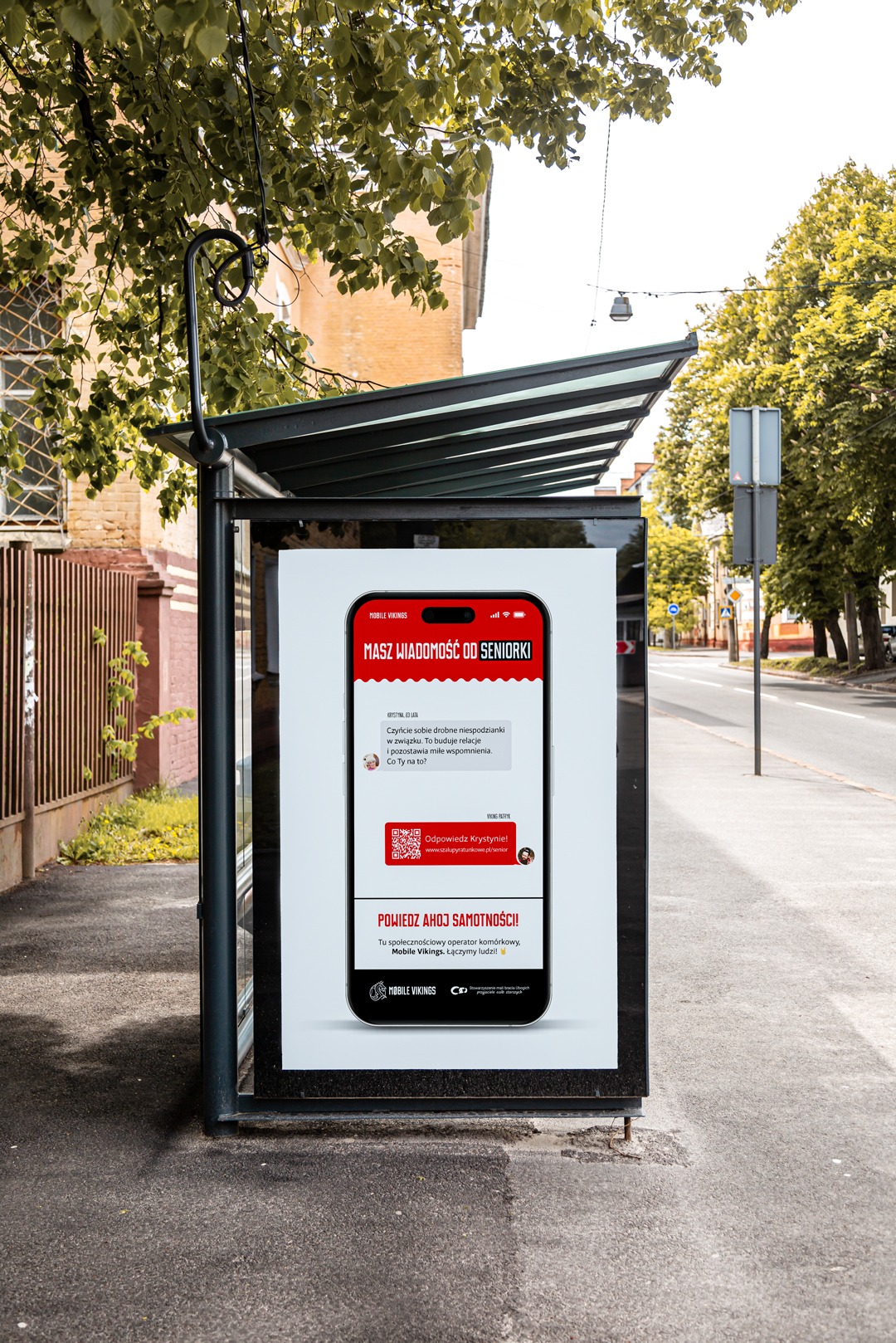 Plakat reklamowy Mobile Vikings na przystanku autobusowym, prezentujący konwersację seniorów w aplikacji, z hasłem 'Powiedz AHOJ samotności!'