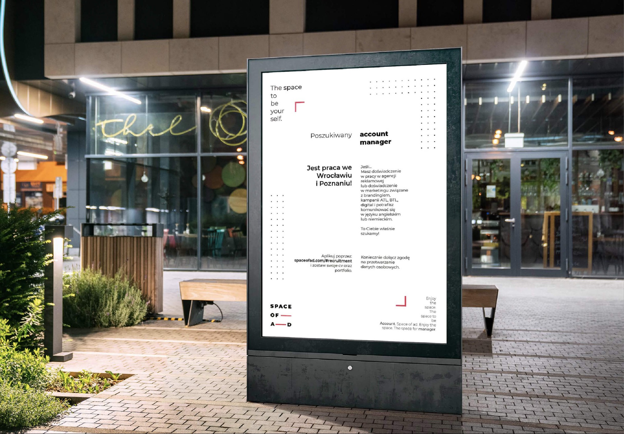 Reklama zewnętrzna na cyfrowym billboardzie z ogłoszeniem o pracę na stanowisko Account Manager w firmie Space of Ad, umieszczona na tle miejskiej przestrzeni z brukowaną nawierzchnią i zielenią.