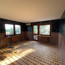 Okay Majster - Pokój po remoncie z wzorzystą podłogą, ciemnymi ścianami z drewnianą boazerią i drabinką malarską w świetle słonecznym.