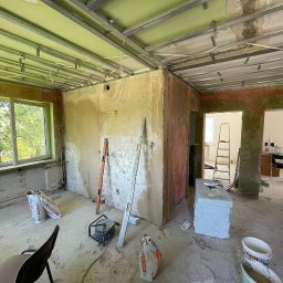 Okay Majster - Wnętrze w trakcie prac w Białymstoku: widoczne profile sufitowe, częściowo wyszpachlowane ściany, poziomice oparta o ścianę, worki z zaprawą i inne narzędzia budowlane.