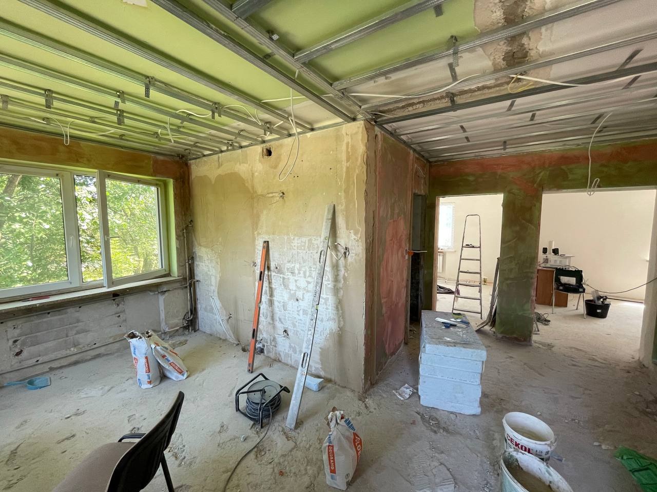 Wnętrze w trakcie prac w Białymstoku: widoczne profile sufitowe, częściowo wyszpachlowane ściany, poziomice oparta o ścianę, worki z zaprawą i inne narzędzia budowlane.