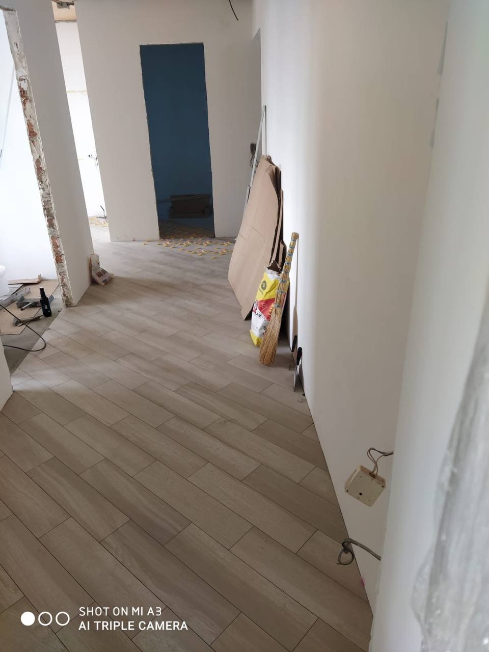 Ułożone panele podłogowe imitujące drewno w trakcie remontu mieszkania, widoczny otwarty pokój z niebieską ścianą w tle oraz materiały budowlane i narzędzia.