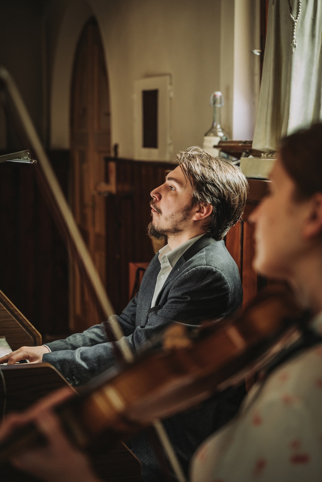 Młody mężczyzna w szarym garniturze gra na organach w kościele, obok niego skrzypaczka podczas ceremonii ślubnej.