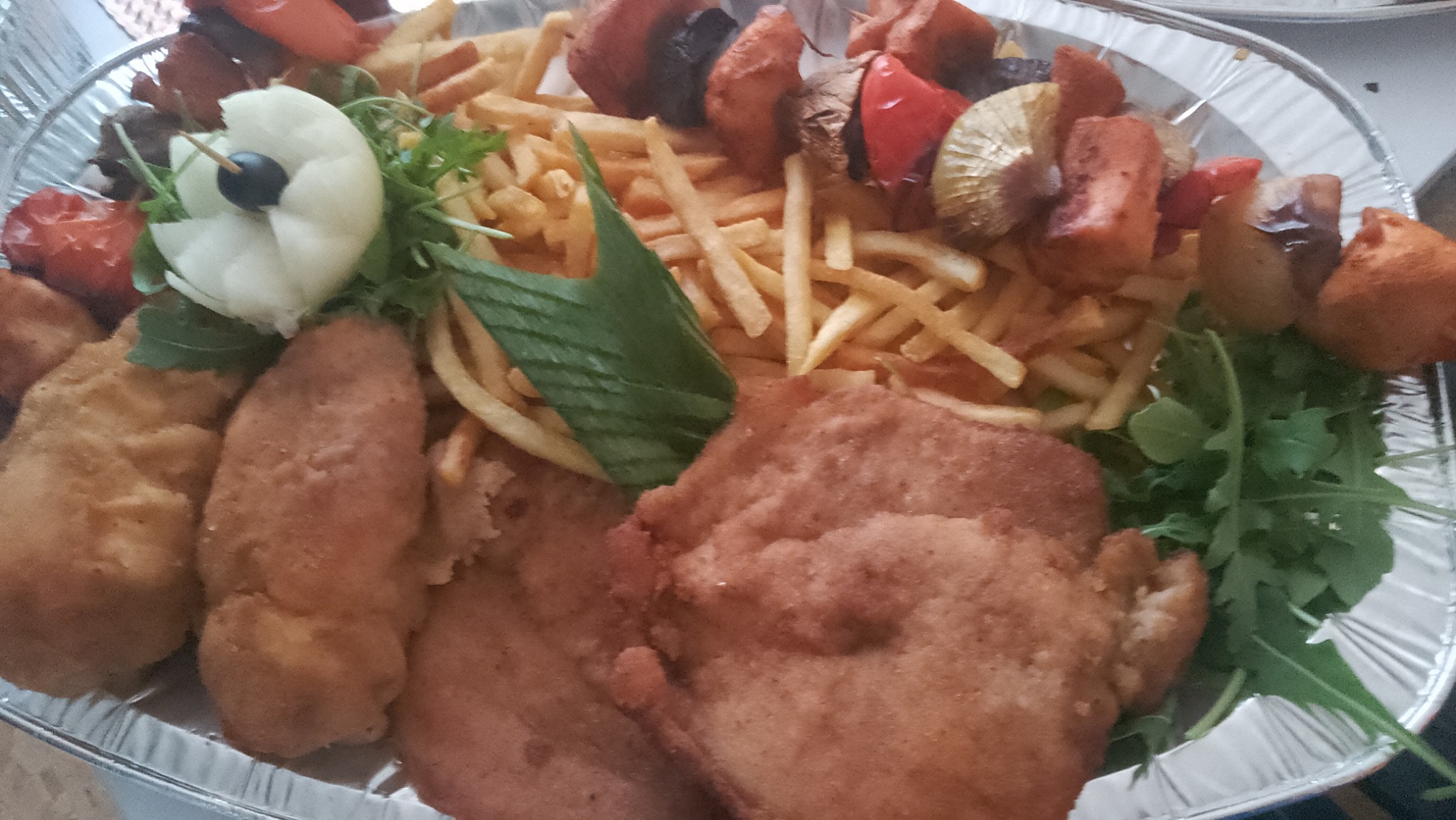 Srebrna taca z frytkami, szaszłykami warzywnymi, kotletami panierowanymi i dekoracją z rucoli oraz kwiatu z białego sera z czarną oliwką.