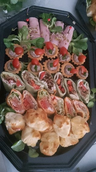 Elegancki catering: Roladki z szynki, tartaletki z pastą, tortille z warzywami i mięsem, oraz mini ptysie na czarnej, ośmiokątnej tacy.