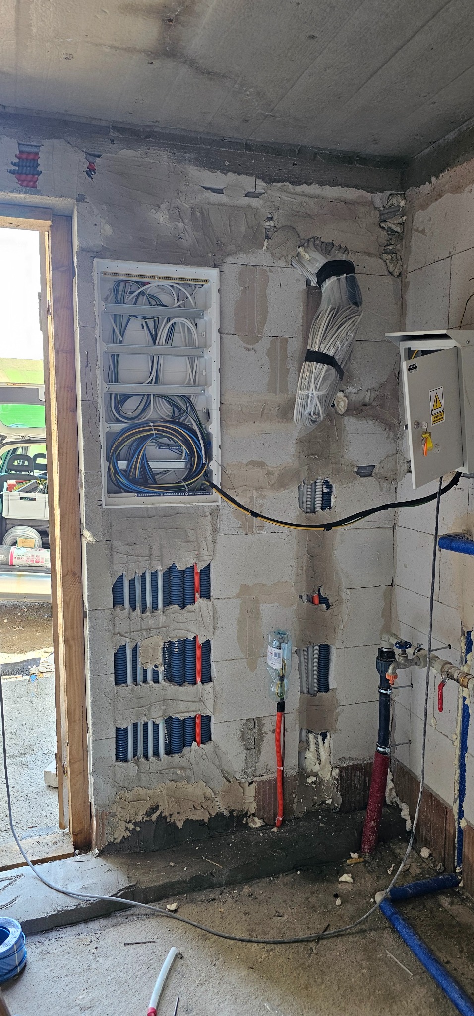Instalacja elektryczna i hydrauliczna w surowym wnętrzu: rozdzielnica z kablami, rury w ścianach, widoczne przewody i elementy instalacji wodnej.