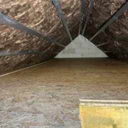 Poddasze z widoczną izolacją z wełny mineralnej między krokwiami, wykończone płytą OSB, z fragmentem ściany z bloczków betonowych w głębi.