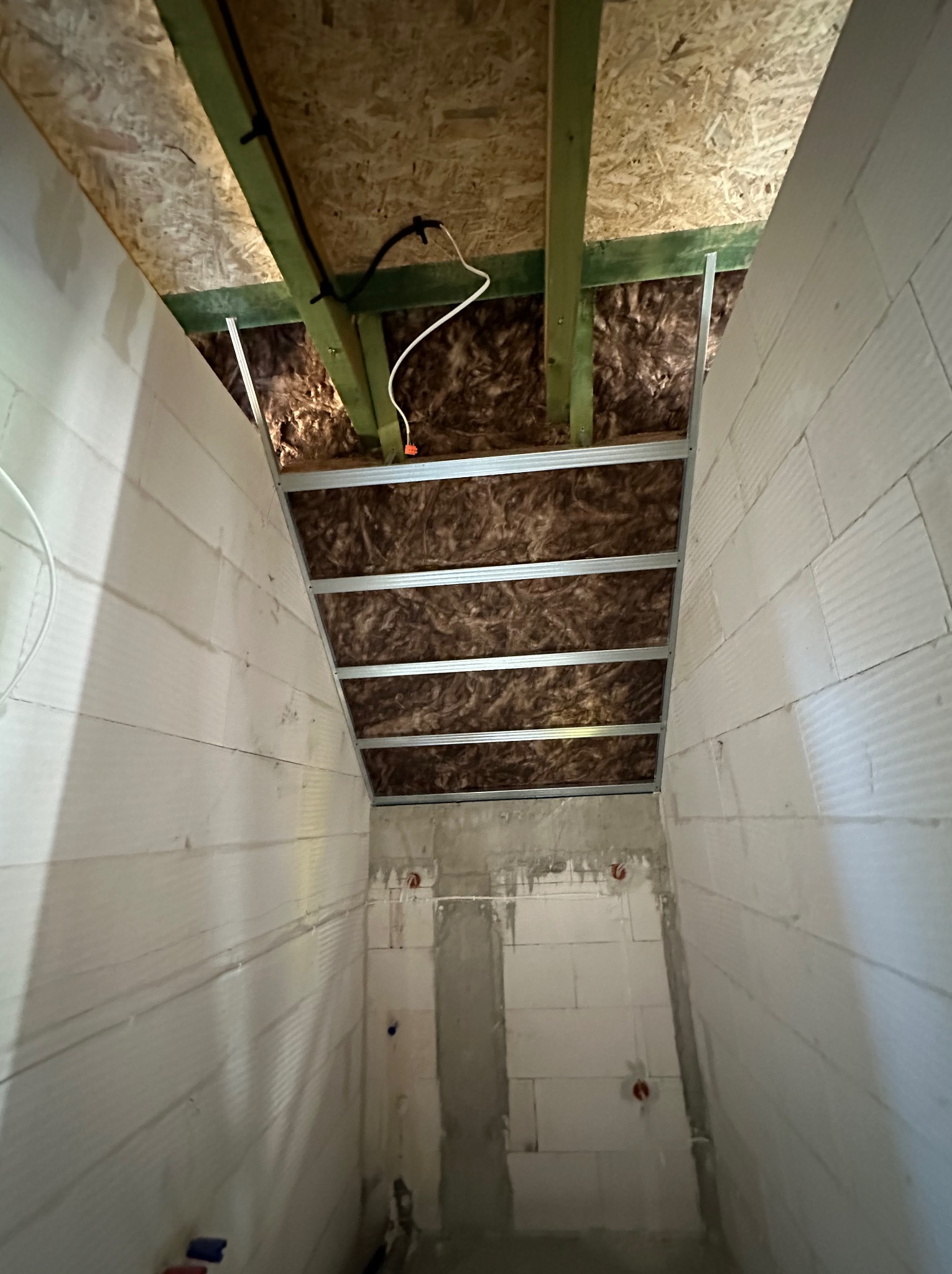 Wnętrze poddasza w trakcie ocieplania wełną mineralną, widoczne profile metalowe do montażu płyt karton-gips i instalacja elektryczna.