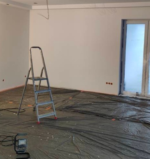 Pokój przed malowaniem: zabezpieczona folią podłoga, drabina malarska, ściany przygotowane do malowania, widoczne kable i puszki elektryczne.