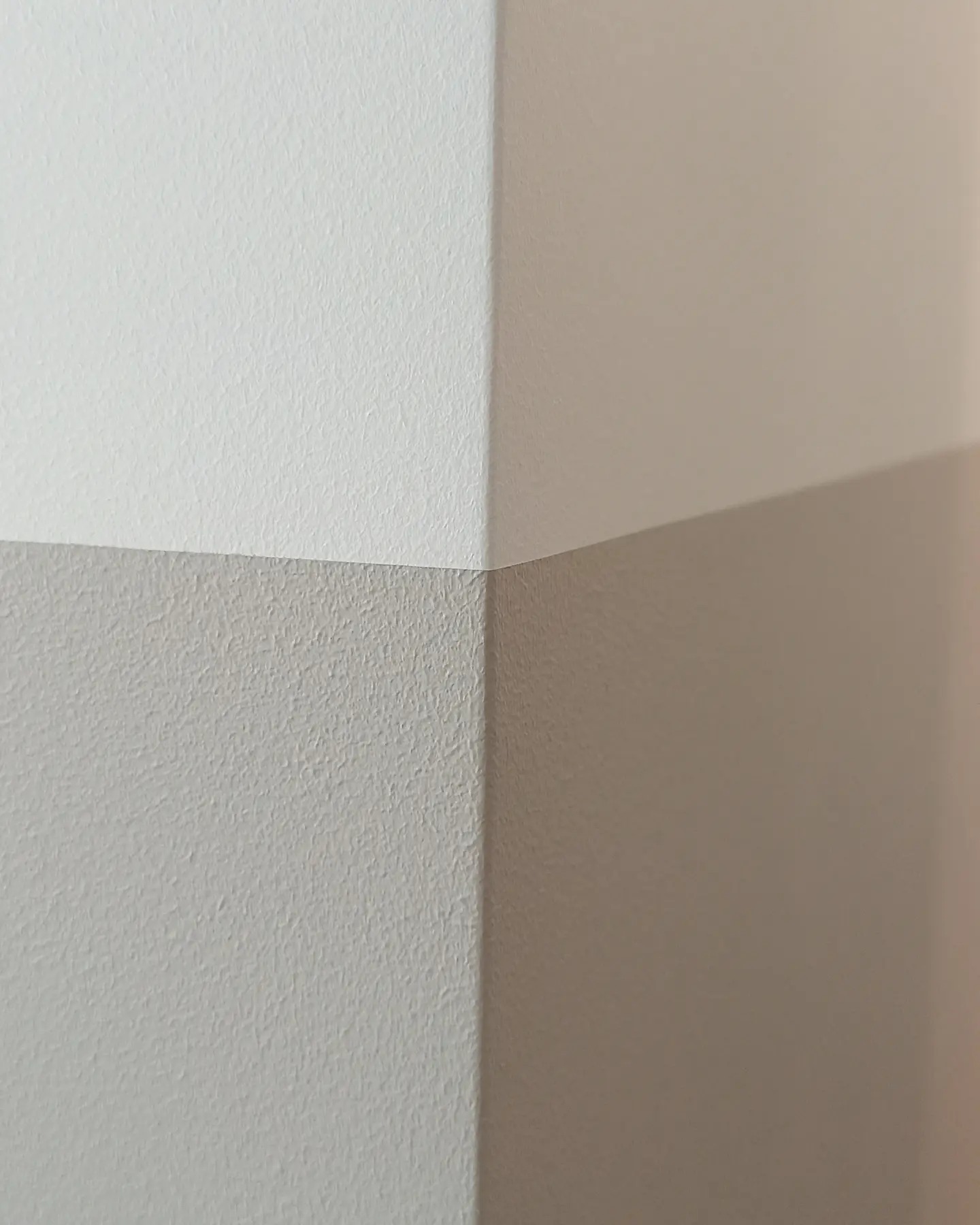 Ściana pomalowana na dwa kolory, biały i beżowy, z widocznym narożnikiem w mieszkaniu w Warszawie.