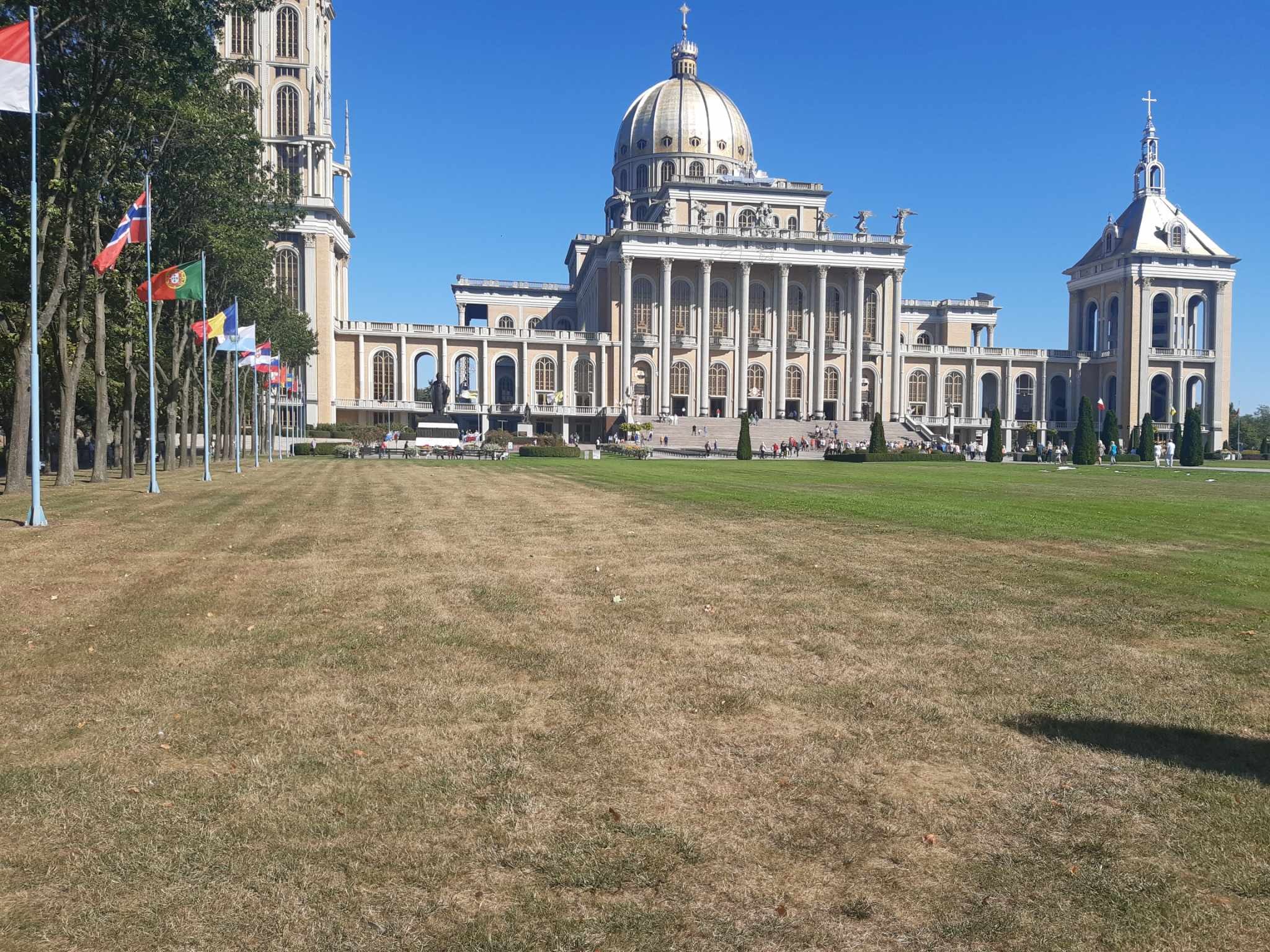 Bazylika w Licheniu Starym z flagami różnych państw wzdłuż ścieżki, widok z dużej odległości na tle błękitnego nieba.