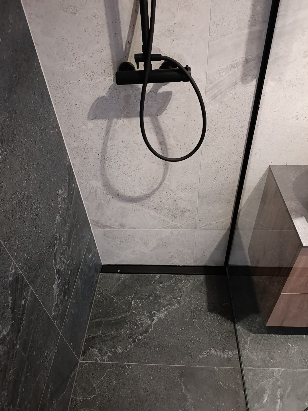 Nowoczesna kabina prysznicowa z czarną armaturą i szarymi płytkami imitującymi marmur, widok z góry, minimalistyczny design.