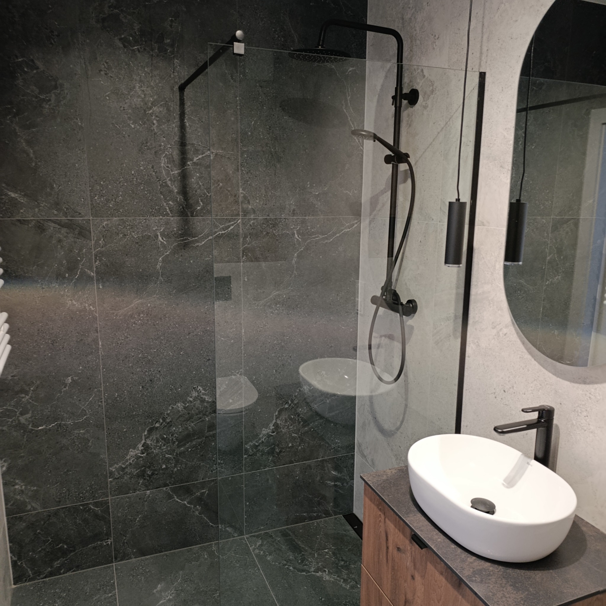Nowoczesna łazienka z kabiną typu walk-in, czarną armaturą i umywalką nablatową. Płytki imitujące kamień w odcieniach szarości. Minimalistyczne oświetlenie.