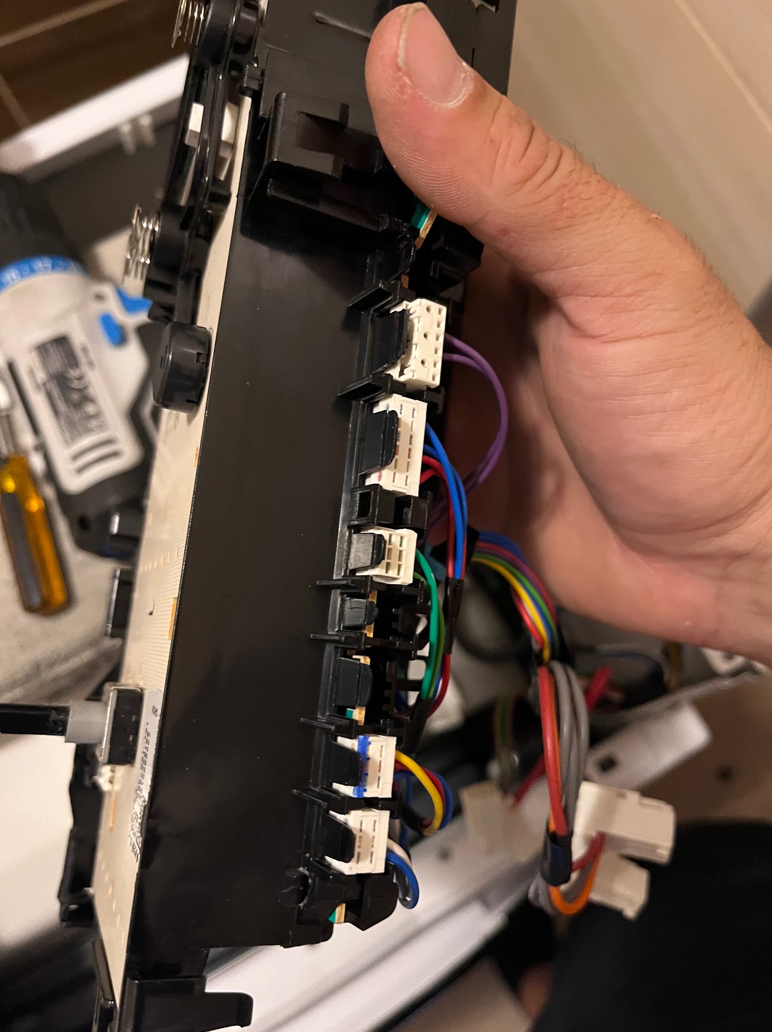 Panel sterowania pralki w trakcie naprawy, widoczne złącza i kolorowe przewody, narzędzia w tle.