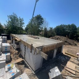 KHRYSTYNA KALYNIAK KALYNIAK BUD - Wylewanie betonu na strop domu w trakcie budowy, widoczna pompa do betonu i pracownicy, ściany z bloczków, szalunki drewniane i zapasy materiałów budowlanych.