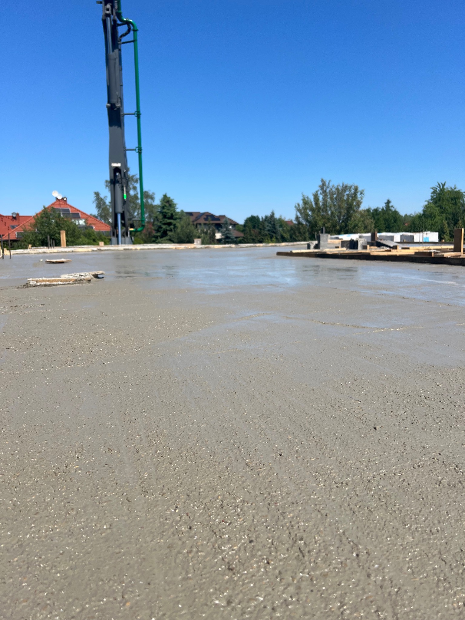 Świeżo wylany, mokry beton na płycie fundamentowej domu jednorodzinnego, widoczny wysięgnik pompy do betonu na tle błękitnego nieba.